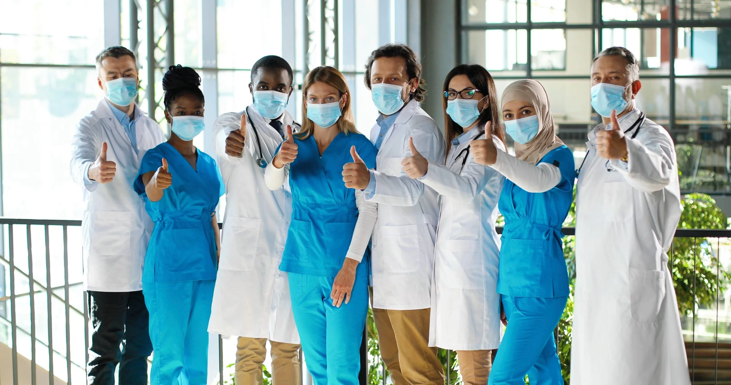 Group of healthcare workers wearing medical masks and uniforms giving thumbs up in a modern clinical setting