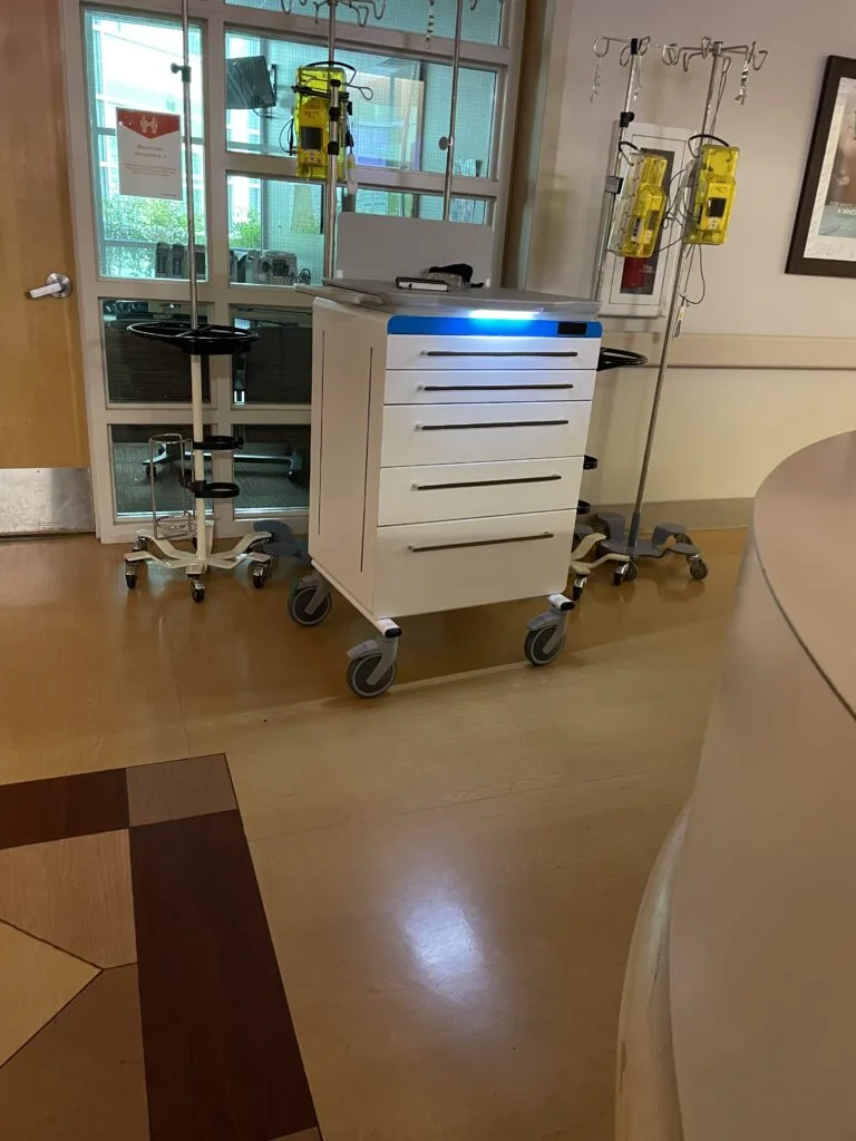 Medical equipment cart with drawers and IV stands in clinical room