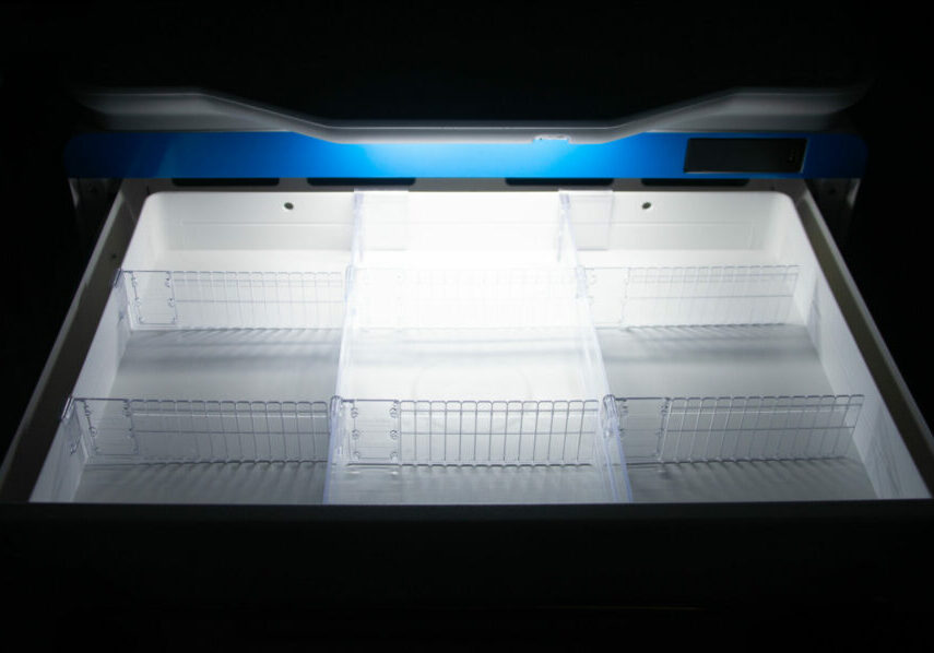 Open freezer chest with blue trim and white wire shelving baskets inside, brightly lit interior against black background.